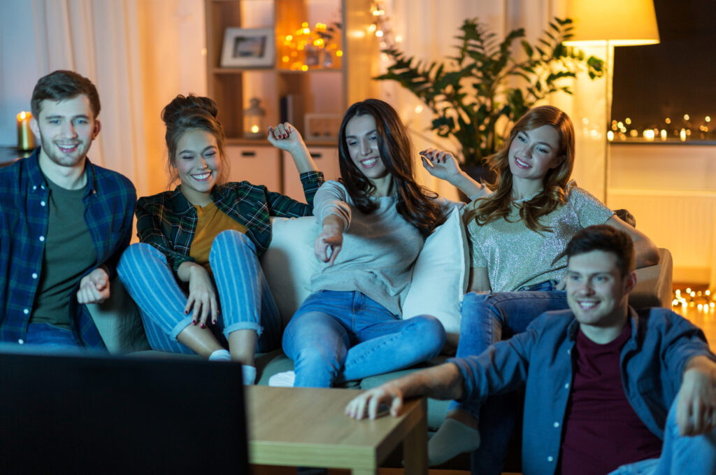 Happy friends watching tv at home in evening