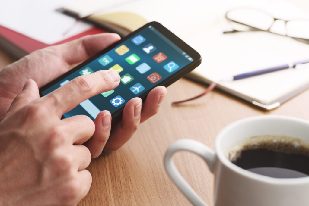 Closeup of male hands touching smartphone screen for using app at table. many application icons on smart phone display.